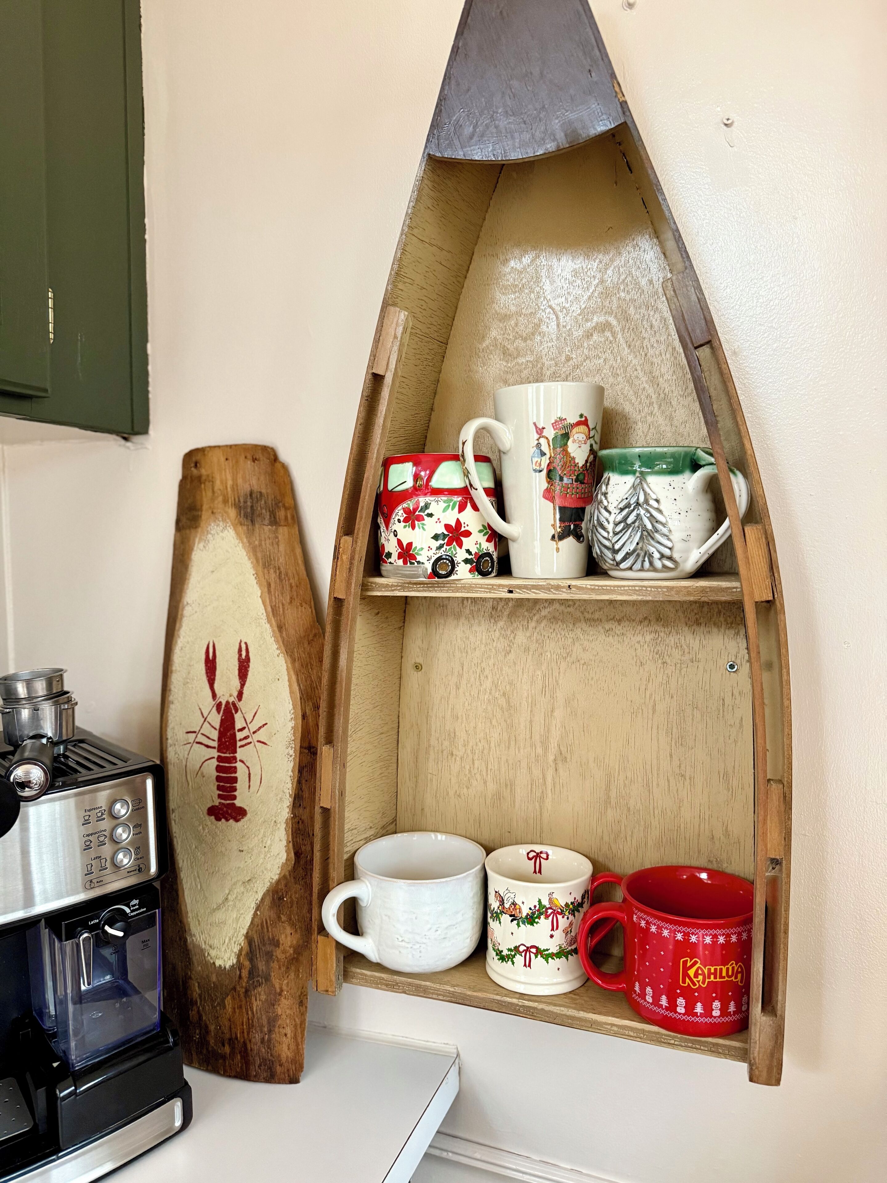 Une cuisine équipée d’une machine à café, décorée d’un homard, et dotée d’une étagère en bois où sont rangées différentes tasses.