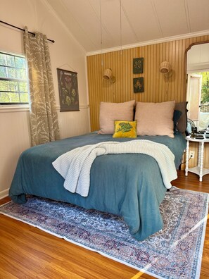A bedroom with a bed, a window with curtains, a wall-mounted lamp, and a patterned rug.