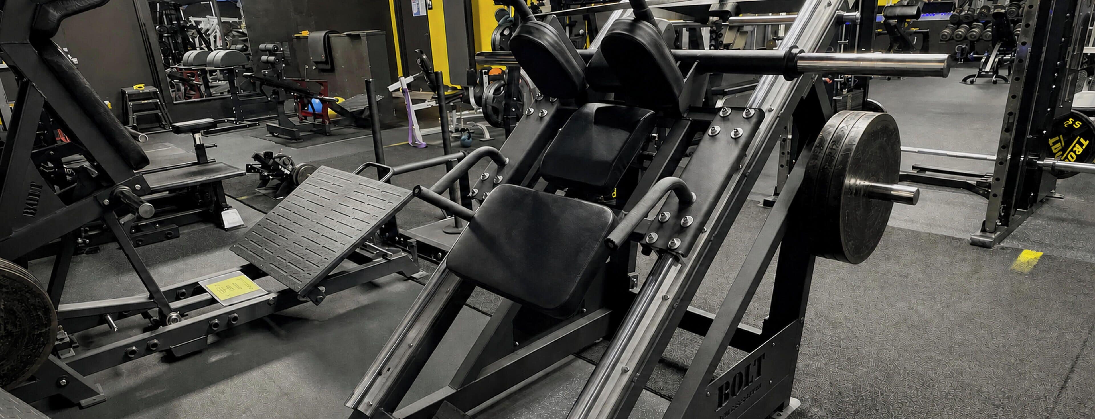 Ein Fitnessraum mit Gewichtstrainern, darunter eine Hantelbank und ein Squat-Stand.