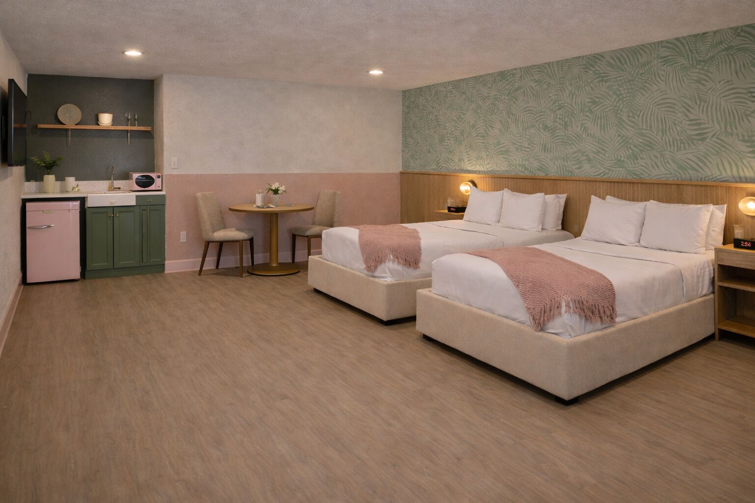 A hotel room with two beds, a small kitchenette, a round table with chairs, and a decorative wall.
