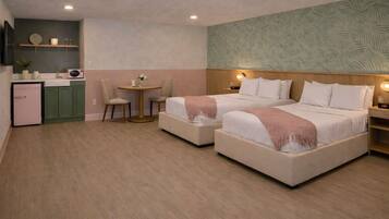 A hotel room with two beds, a small kitchenette, a round table with chairs, and a decorative wall.