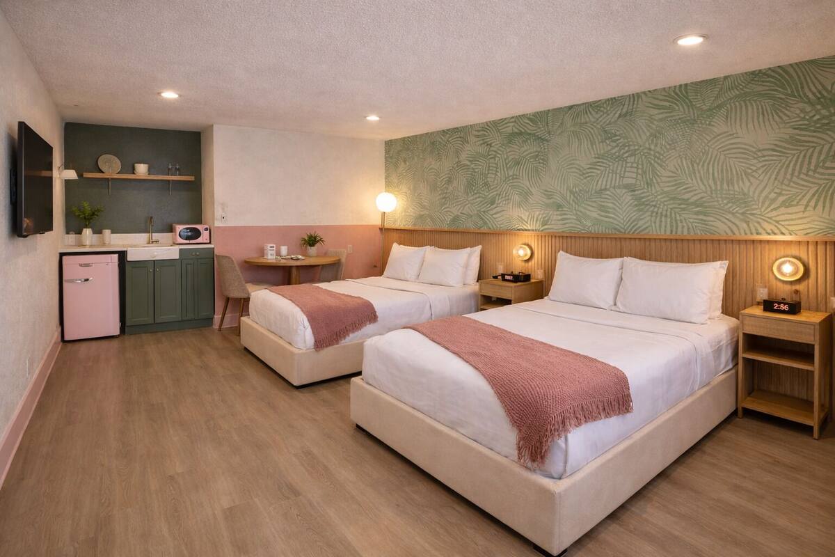 A hotel room with two beds, a kitchenette, a small dining table, and a bathroom.