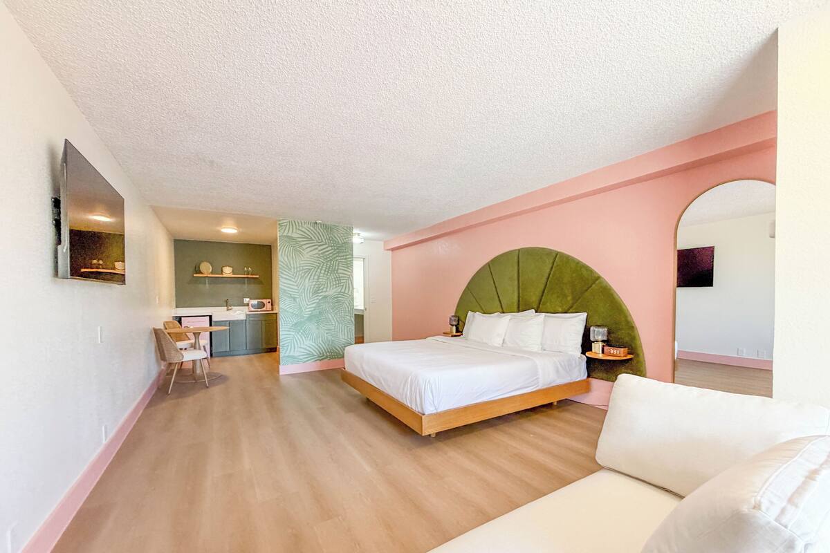A modern bedroom with a bed, a small desk, and a kitchenette area.