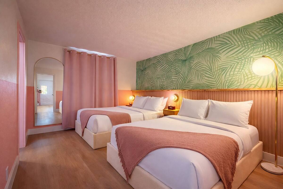 A hotel room with two beds, a mirror, a wall with a leaf pattern, and a floor lamp.