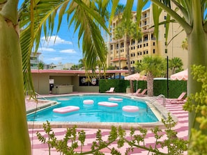 Zona de piscina con sillones de descanso, un bar y un edificio al fondo.
