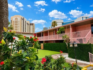 Un hotel con césped verde, un edificio rosa y una palmera.