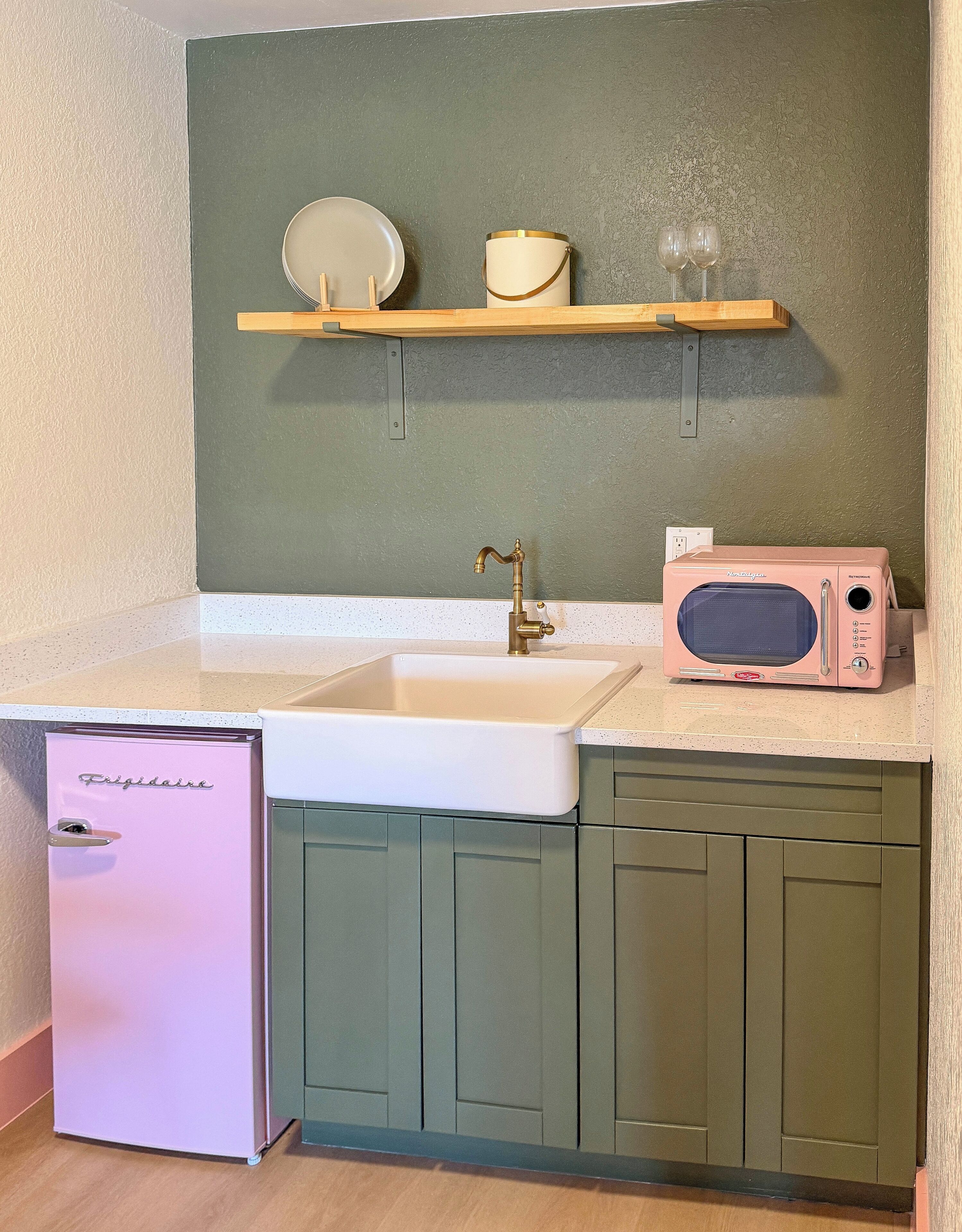 A compact kitchen with a sink, a pink refrigerator, and a microwave on the countertop.