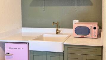 A compact kitchen with a sink, a pink refrigerator, and a microwave on the countertop.