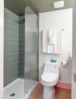 Un baño con ducha acristalada, inodoro blanco y barra para toallas.