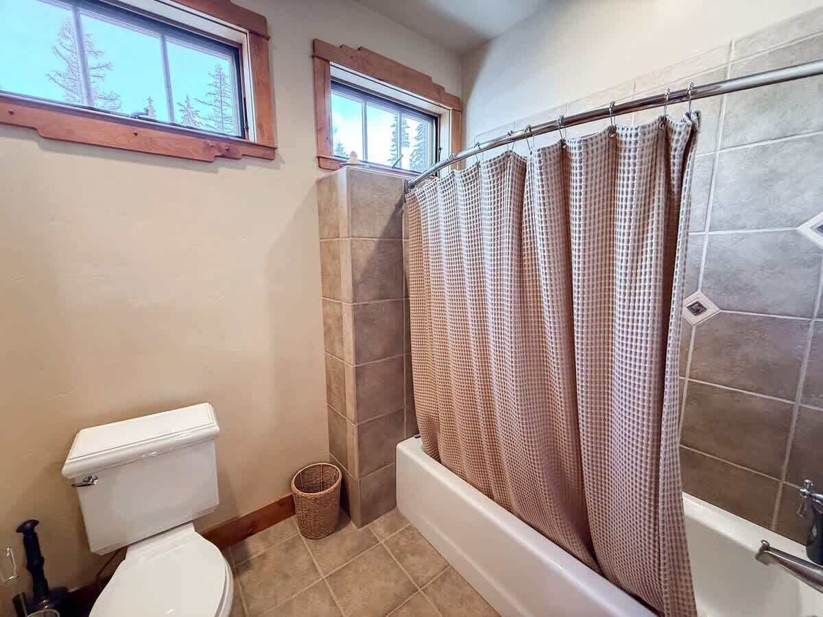 Une salle de bain avec des toilettes, une douche dotée d’un rideau à carreaux et une fenêtre située au-dessus des toilettes.