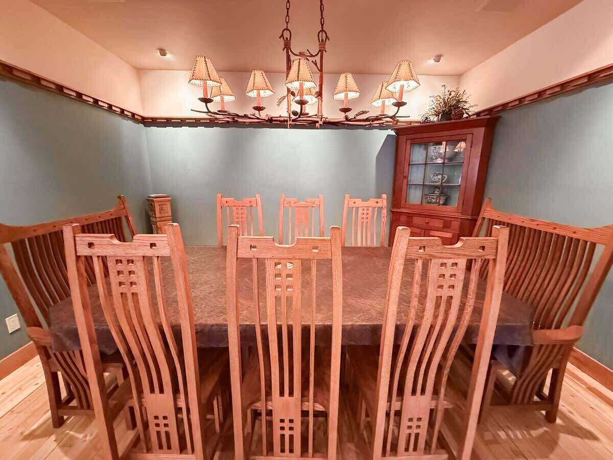Comedor con mesa y sillas de madera, una araña y un aparador con puertas de vidrio.