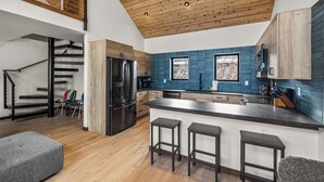 A modern kitchen with a large island, wooden ceiling, and blue backsplash. - Downtown Whitefish Retreat – Hot Tub • Mountain Views • 3 Bedrooms + sleeping Loft (Whitefish)