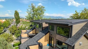 A modern multi-story building with a rooftop deck, large windows, and a view of the surrounding area. - Downtown Whitefish Retreat – Hot Tub • Mountain Views • 3 Bedrooms + sleeping Loft (Whitefish)