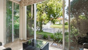 A patio with a glass table and chairs, overlooking a garden with a fountain and trees. - Welcome To Your Naples Escape, Perfectly Situated In One Of The Most Desirable Areas Of Town! (Naples)