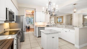 A modern kitchen with white cabinetry, stainless steel appliances, a marble countertop, and a chandelier. - Welcome To Your Naples Escape, Perfectly Situated In One Of The Most Desirable Areas Of Town! (Naples)