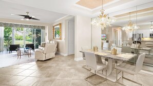 A spacious dining area with a marble table and white chairs, a ceiling fan, and a large chandelier. - Welcome To Your Naples Escape, Perfectly Situated In One Of The Most Desirable Areas Of Town! (Naples)