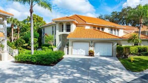 A two-story house with a red-tiled roof, a white garage door, and a well-maintained front yard with palm trees and shrubs. - Welcome To Your Naples Escape, Perfectly Situated In One Of The Most Desirable Areas Of Town! (Naples)