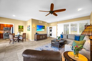 A spacious living area with a ceiling fan, a kitchen with modern appliances, a dining area, and a seating area with a sofa and coffee table. - Kapalua Bay Villas | Oceanfront 1 BR | Car Incl. w/ 6+ Nights | KBV-35G2 by KBM (Lahaina)