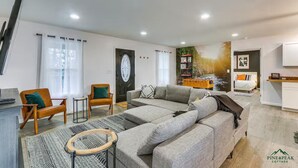 A modern living room with a grey sectional sofa, two armchairs, a coffee table, and a small side table. There is a bookshelf with books and decorative items, a door with a decorative glass panel, and a wall-mounted TV. - PINE PEAK COTTAGE: Quiet Luxury in the Mountains of Bryce Resort (Mount Jackson)