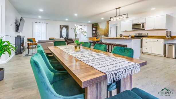 A modern living room with a wooden dining table, teal chairs, and a large window with curtains. - PINE PEAK COTTAGE: Quiet Luxury in the Mountains of Bryce Resort (Mount Jackson)