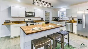 A modern kitchen with white cabinets, a central island with stools, stainless steel appliances, and a hanging light fixture. - PINE PEAK COTTAGE: Quiet Luxury in the Mountains of Bryce Resort (Mount Jackson)