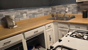 Una cocina con estufa a gas, cafetera, lavamanos y alacenas.