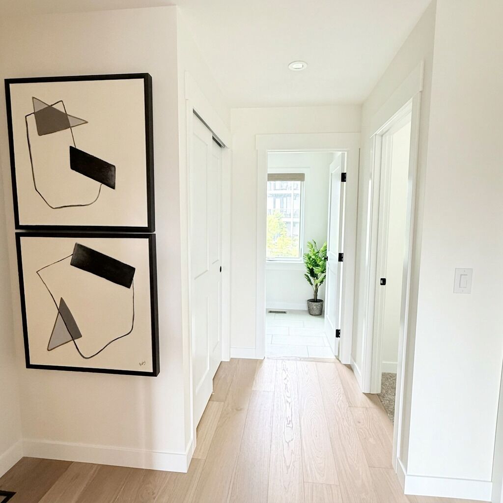 Un pasillo con dos obras de arte abstracto enmarcadas en la pared, una planta en maceta y una puerta que da a otra habitación.