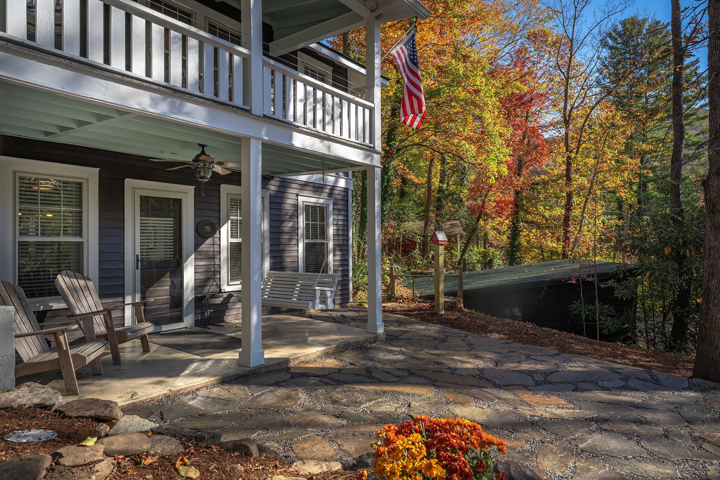A two-story house with a porch, a flag, and a stone pathway.