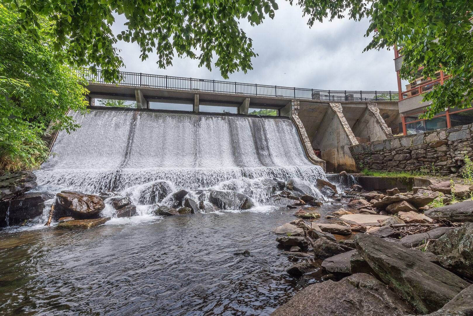 A waterfall cascading over rocks into a river, with a bridge and stone walls in the background.