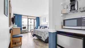 Et hotelværelse med seng, skrivebord, stol, tekøkken og udsigt ud