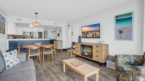 En moderne stue med pejs, spiseplads og et køkken i baggrunden.