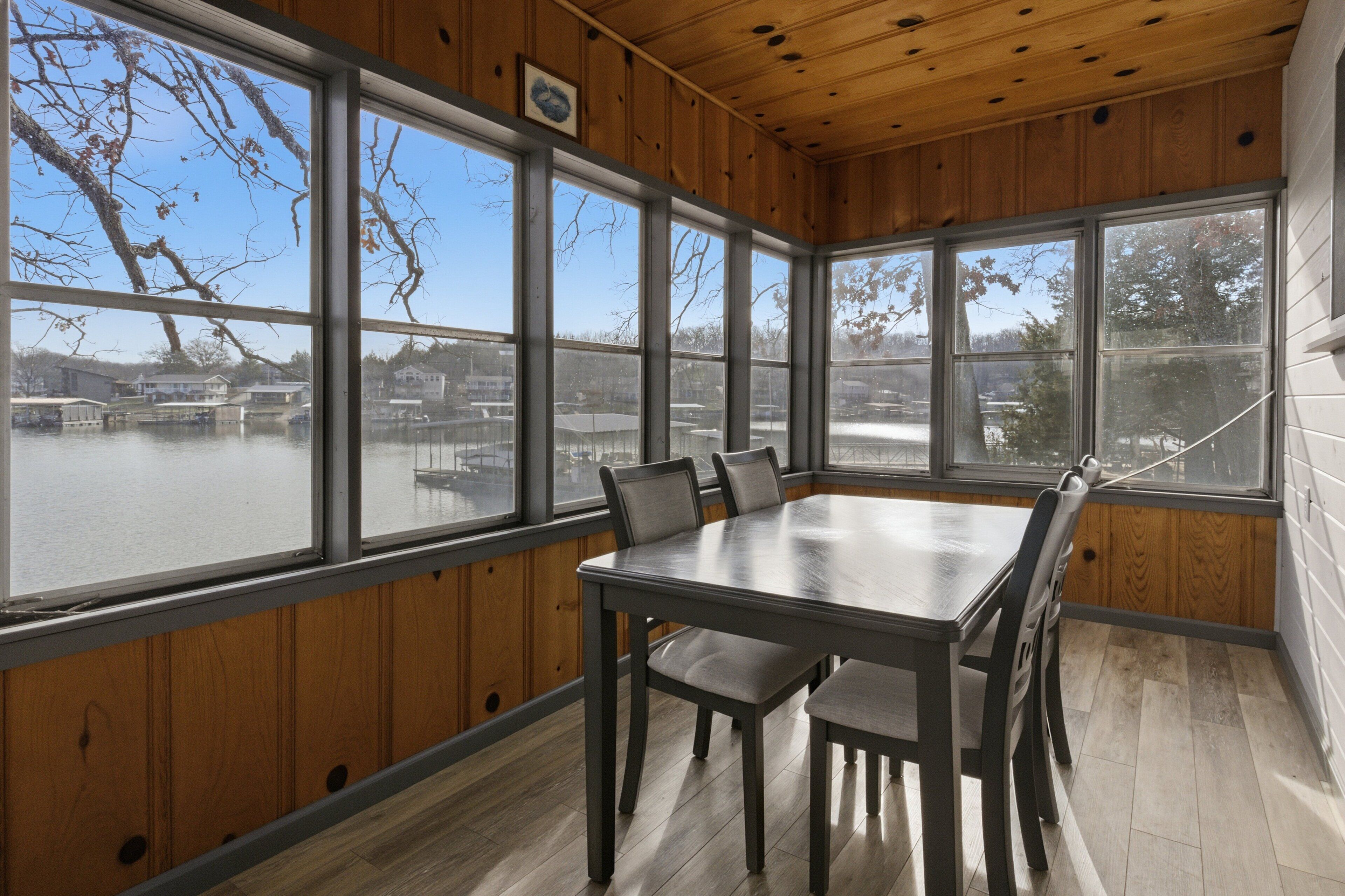 A sunroom with a large table and chairs, wooden walls, and large windows overlooking a snowy landscape.