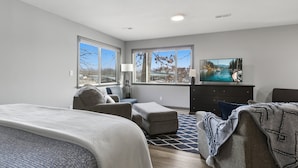 Ein modernes Schlafzimmer mit einem großen Bett, einer Couch, einem Fernseher und Blick auf einen Fluss durch große Fenster.