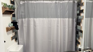 Ein Badezimmer mit Toilette, schwarzem Waschbecken mit breiter Spüle, einer Duschvorhang und einer Deckenleuchte.