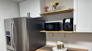 Eine moderne Küche mit einem Edelstahl-Kühlschrank, einer Mikrowelle und einer Kaffeemaschine auf einem Holzregal.