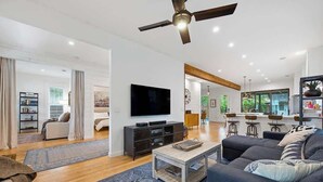 Una sala de estar moderna con televisor de pantalla plana, sofá oscuro, una mesa de centro y ventilador de techo.