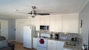 A compact kitchen with white cabinets, a refrigerator, a microwave, a stove, and a ceiling fan.