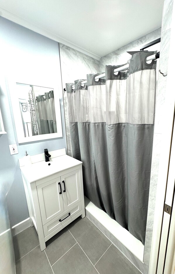 A bathroom with a white vanity, a mirror, and a shower curtain. - Serene 1-bedroom Cottage with Beach Access! "Where The Coast is Calling!" (St. Pete Beach)