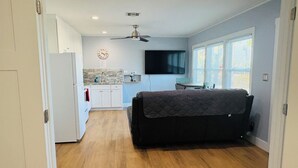 A compact living space with a kitchenette, a sofa, a ceiling fan, and a TV.