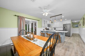 Una cocina moderna con armarios blancos, una isla central y un comedor con mesa y sillas de madera.