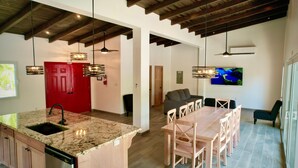 A modern kitchen with a granite countertop, a red door, and a dining area with a wooden table and chairs. - Compass Rose House at Ceiba Beach Resort (Placencia)