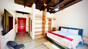 A bedroom with a bed, a TV, a red door, and a wooden ceiling. - Compass Rose House at Ceiba Beach Resort (Placencia)