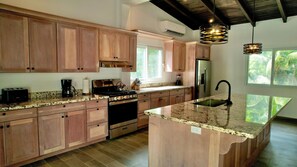 A kitchen with wooden cabinets, a stainless steel refrigerator, a stove, and a granite countertop. - Compass Rose House at Ceiba Beach Resort (Placencia)