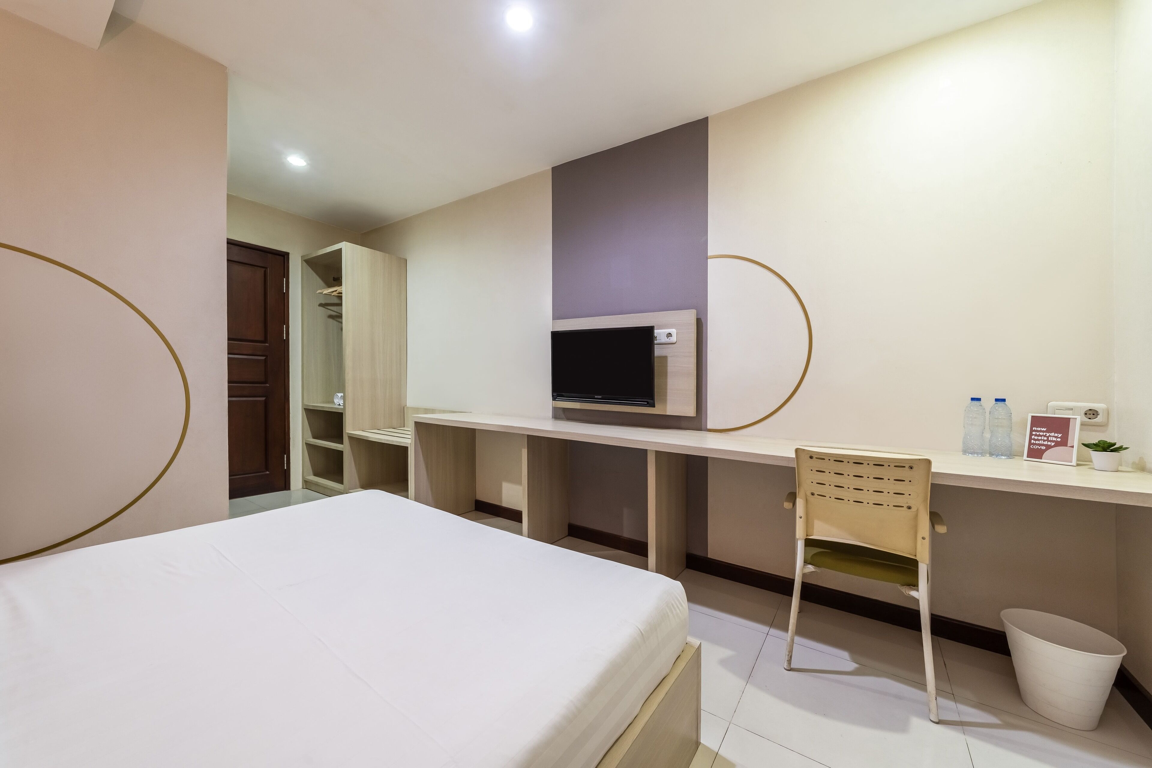 Una habitación de hotel con cama, escritorio con televisor, silla, cesto de basura y armario.