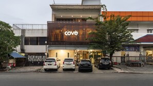 Ein modernes Gebäude mit einem 'Cove'-Schild, mehreren parkenden Autos und einem Baum davor.