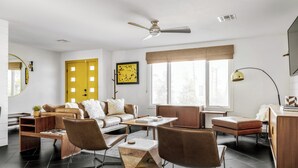 A modern living room with a sofa, coffee table, and chairs. There is a window with a view, a ceiling fan, and a yellow door. - Bello Grove | Old Town w/ Pool, Putting Green, Pinball & Games (Scottsdale)