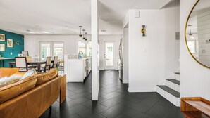 A modern kitchen with white cabinets, a central island, and a dining area with a brown leather couch. - Bello Grove | Old Town w/ Pool, Putting Green, Pinball & Games (Scottsdale)