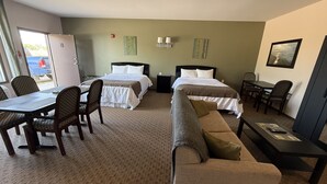 Ein Hotelzimmer mit zwei Betten, einem Esstisch, Stühlen, einer Couch, einem Fernseher und einem kleinen Tisch mit Fernbedienung.