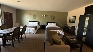 Ein Hotelzimmer mit zwei Betten, einer Couch, einem Esstisch mit Stühlen, einem kleinen Schreibtisch und einem Kleiderschrank.