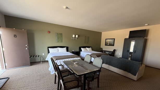 Ein Hotelzimmer mit zwei Betten, einem Esstisch mit Stühlen, einem Fernseher und einem Kleiderschrank.